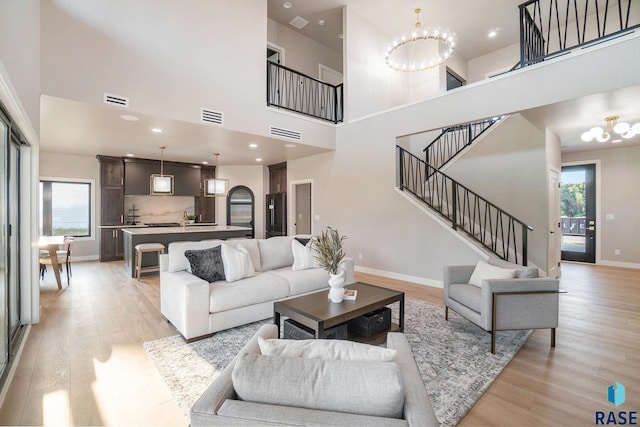 living room featuring a high ceiling, a healthy amount of sunlight, light hardwood / wood-style floors, and an inviting chandelier