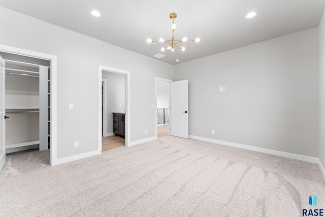 unfurnished bedroom with light carpet, an inviting chandelier, a closet, and a spacious closet