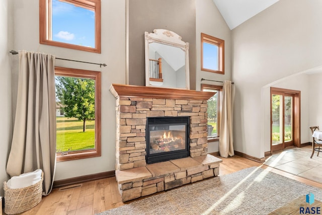 living room with light hardwood / wood-style floors, high vaulted ceiling, a healthy amount of sunlight, and a stone fireplace