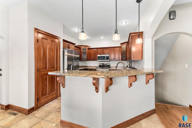 kitchen with appliances with stainless steel finishes, kitchen peninsula, decorative light fixtures, and light stone countertops