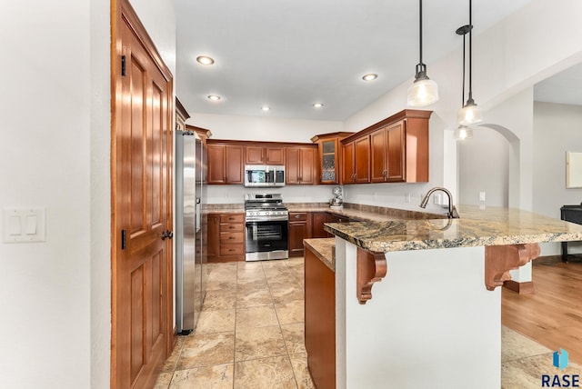 kitchen with dark stone countertops, decorative light fixtures, a kitchen breakfast bar, kitchen peninsula, and appliances with stainless steel finishes