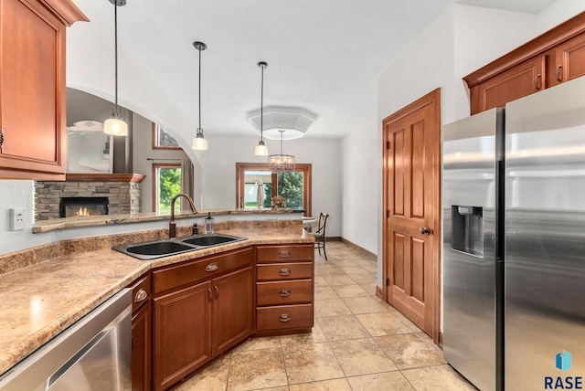 kitchen featuring pendant lighting, light tile patterned floors, stainless steel appliances, sink, and a stone fireplace