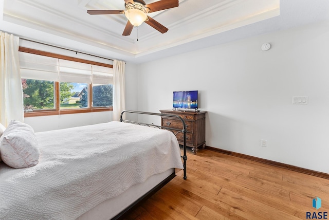 bedroom with ceiling fan, a raised ceiling, wood-type flooring, and ornamental molding