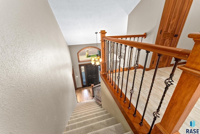 staircase featuring lofted ceiling, wood-type flooring, and a chandelier