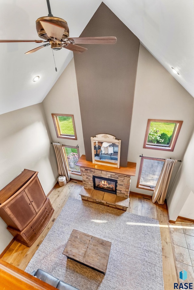 living room with light wood-type flooring, ceiling fan, high vaulted ceiling, and a fireplace