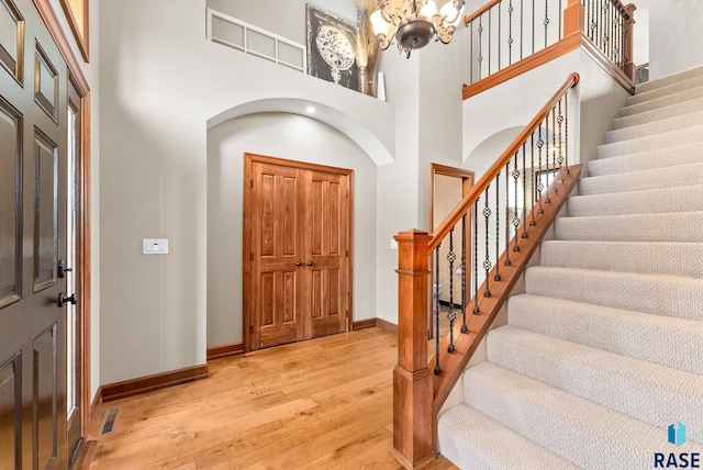 entrance foyer with light hardwood / wood-style flooring, a towering ceiling, and a notable chandelier