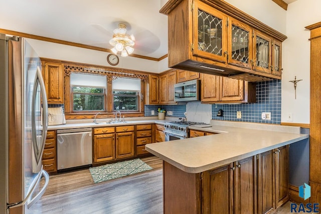 kitchen with light hardwood / wood-style floors, sink, kitchen peninsula, stainless steel appliances, and ornamental molding