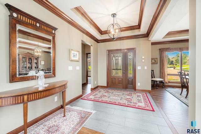 entryway with crown molding, a tray ceiling, and a chandelier