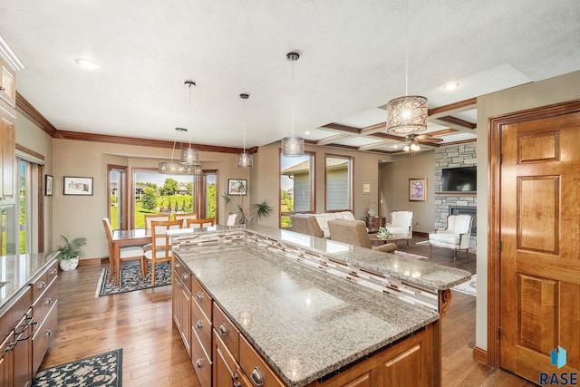 kitchen with decorative light fixtures, coffered ceiling, a center island, light stone countertops, and light wood-type flooring