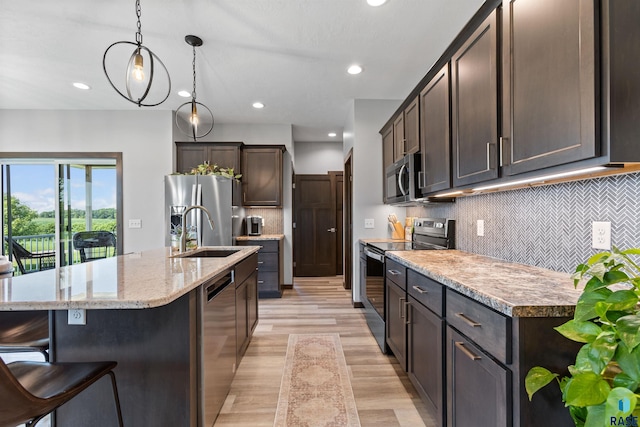 kitchen with stainless steel appliances, light wood-style flooring, a sink, dark brown cabinets, and an island with sink