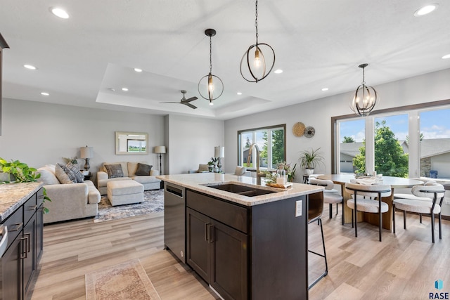 kitchen featuring stainless steel dishwasher, light wood-style flooring, a sink, dark brown cabinets, and decorative light fixtures