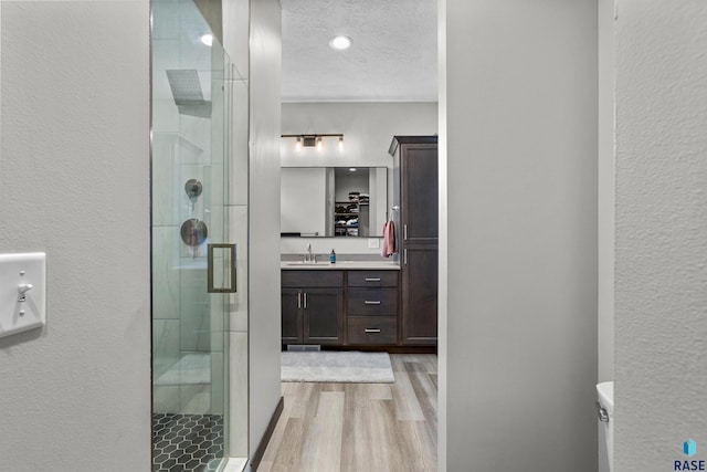 bathroom with a shower stall, a textured wall, vanity, and wood finished floors