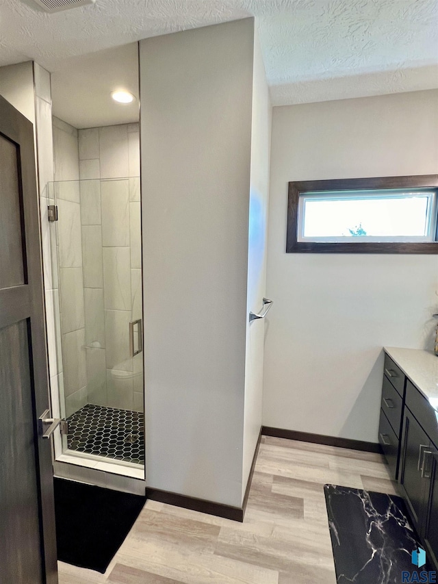 full bath featuring wood finished floors, vanity, baseboards, a textured ceiling, and a stall shower