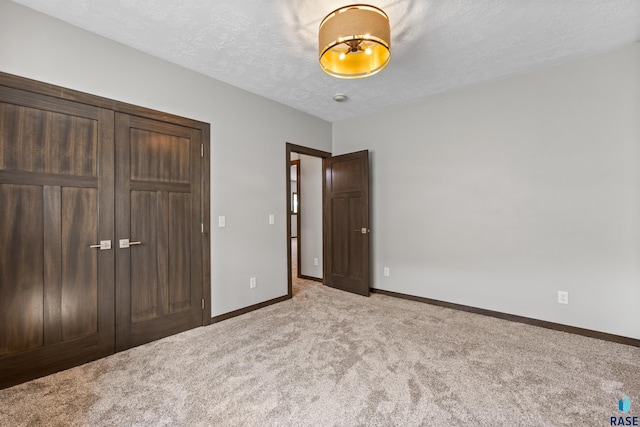 unfurnished bedroom with baseboards, a textured ceiling, a closet, and light colored carpet