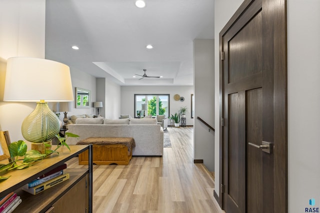 hall with light wood-style flooring, a tray ceiling, recessed lighting, and an upstairs landing