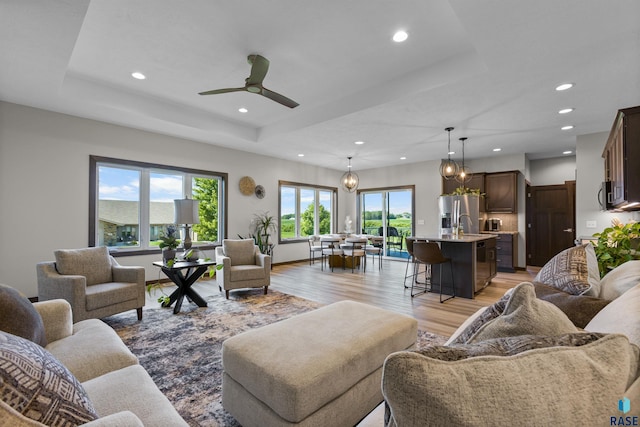 living area featuring ceiling fan with notable chandelier, recessed lighting, light wood-style floors, and a raised ceiling