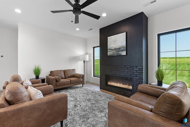 living room with wood finished floors, a glass covered fireplace, ceiling fan, visible vents, and recessed lighting