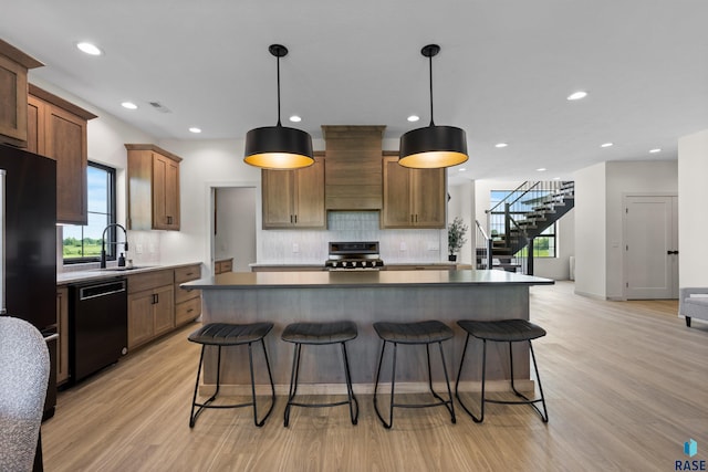 kitchen with light wood finished floors, decorative backsplash, custom range hood, dishwasher, and range