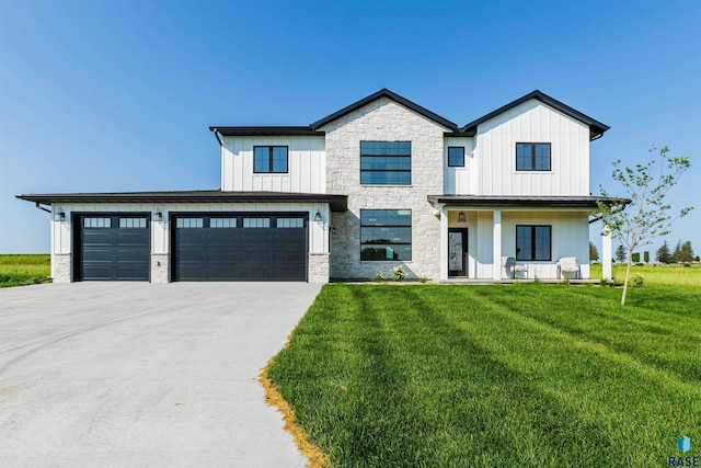 modern farmhouse style home with a front lawn, driveway, stone siding, a porch, and board and batten siding
