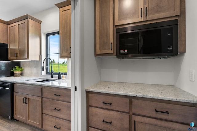 kitchen with tasteful backsplash, light stone countertops, a sink, and black appliances