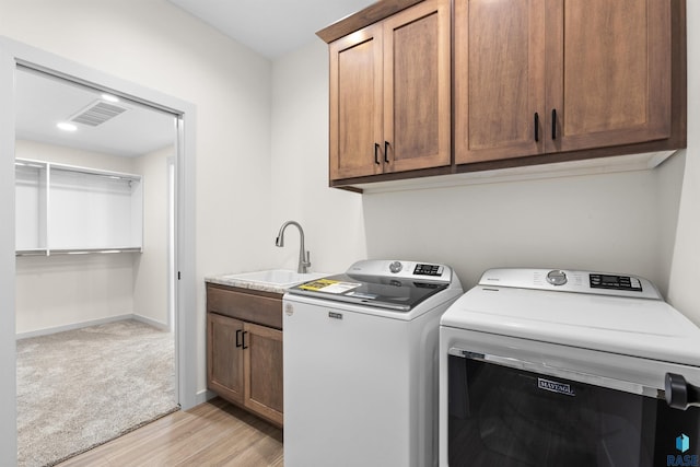 washroom featuring light wood finished floors, a sink, washing machine and dryer, visible vents, and cabinet space