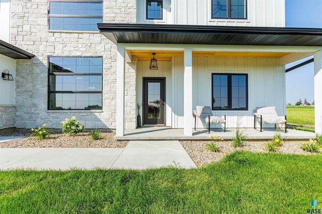 view of exterior entry featuring a porch, board and batten siding, stone siding, and a yard
