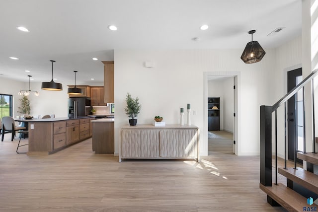 kitchen with recessed lighting, light wood finished floors, high end black fridge, brown cabinetry, and a breakfast bar area