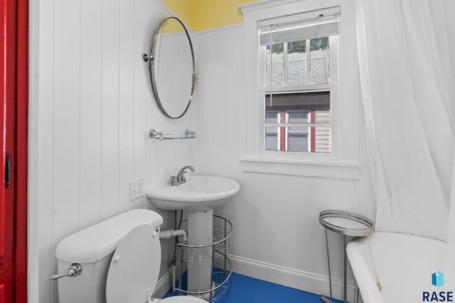 bathroom featuring sink, wood walls, toilet, and a bath