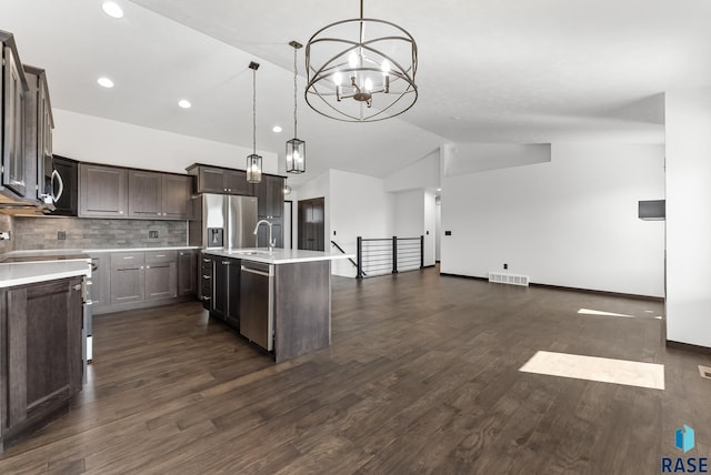 kitchen with appliances with stainless steel finishes, dark hardwood / wood-style flooring, pendant lighting, and an island with sink