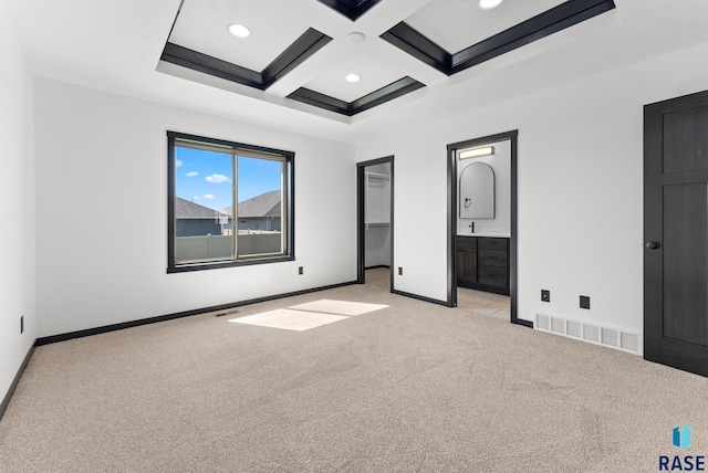 unfurnished bedroom featuring beam ceiling, light colored carpet, coffered ceiling, connected bathroom, and a spacious closet