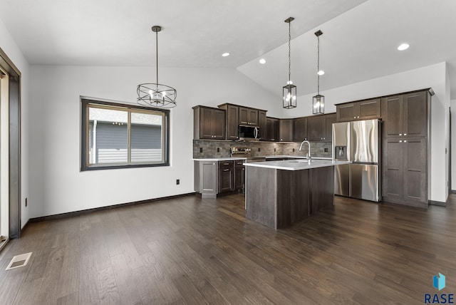 kitchen with pendant lighting, a kitchen island with sink, dark wood-type flooring, vaulted ceiling, and appliances with stainless steel finishes