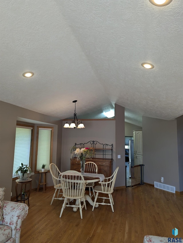 dining area with dark hardwood / wood-style floors, vaulted ceiling, a textured ceiling, and a notable chandelier