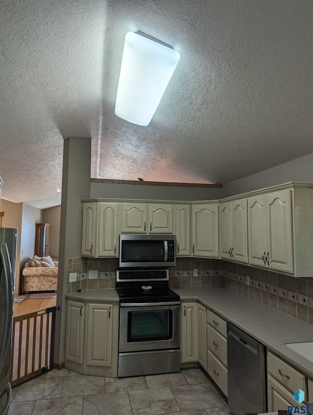 kitchen with cream cabinets, decorative backsplash, stainless steel appliances, and a textured ceiling