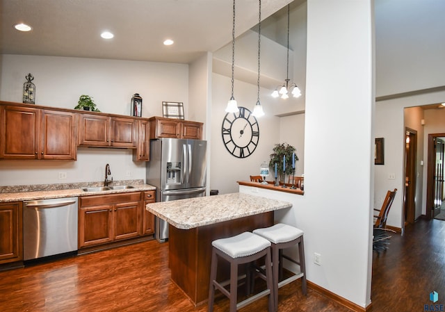 kitchen with a breakfast bar, sink, appliances with stainless steel finishes, decorative light fixtures, and dark hardwood / wood-style flooring