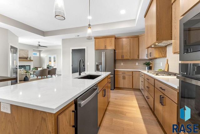 kitchen featuring appliances with stainless steel finishes, hanging light fixtures, light hardwood / wood-style floors, a center island with sink, and sink