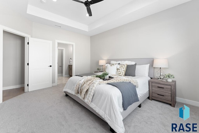 carpeted bedroom with a raised ceiling, ceiling fan, and ensuite bathroom