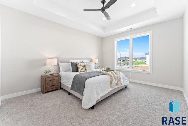 carpeted bedroom with ceiling fan and a tray ceiling