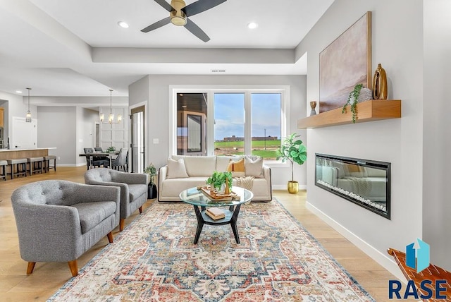 living room with light wood-type flooring and ceiling fan with notable chandelier