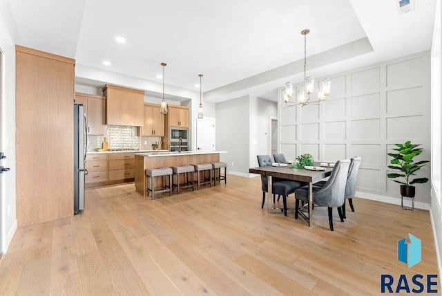 dining space with an inviting chandelier, light wood-type flooring, and sink