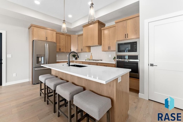 kitchen featuring hanging light fixtures, sink, stainless steel appliances, light brown cabinetry, and light wood-type flooring