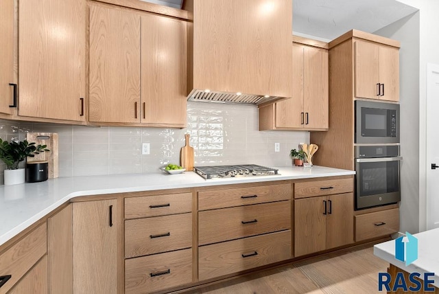 kitchen featuring custom exhaust hood, light hardwood / wood-style flooring, stainless steel appliances, backsplash, and light brown cabinetry