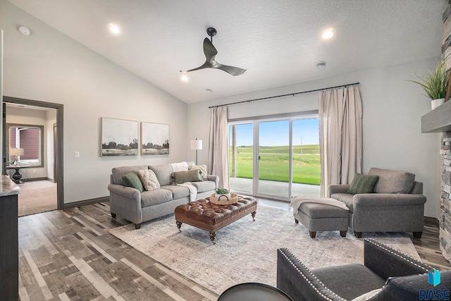 living room featuring a textured ceiling, hardwood / wood-style flooring, a fireplace, high vaulted ceiling, and ceiling fan