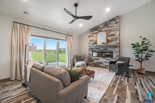 living room featuring a textured ceiling, high vaulted ceiling, hardwood / wood-style floors, a stone fireplace, and ceiling fan