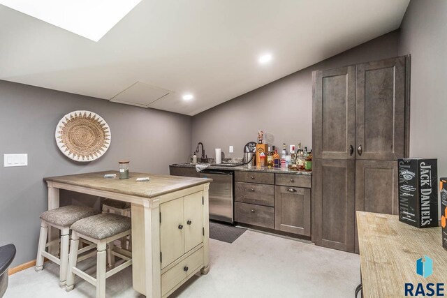 kitchen featuring dark brown cabinetry, lofted ceiling, dishwasher, a breakfast bar, and light colored carpet