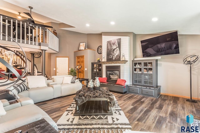 living room featuring a large fireplace, dark wood-type flooring, and ceiling fan