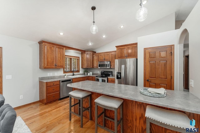 kitchen featuring stainless steel appliances, lofted ceiling, a kitchen breakfast bar, pendant lighting, and light hardwood / wood-style flooring