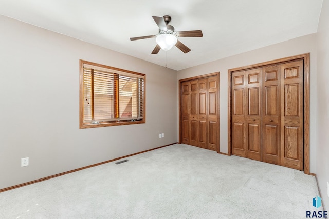 unfurnished bedroom featuring ceiling fan, light carpet, and two closets