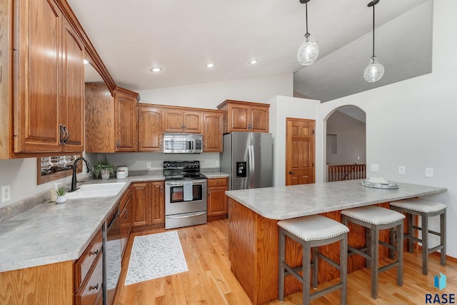 kitchen featuring stainless steel appliances, vaulted ceiling, sink, pendant lighting, and light hardwood / wood-style flooring