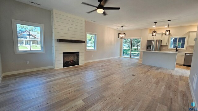 unfurnished living room with a wealth of natural light, light hardwood / wood-style floors, a fireplace, and ceiling fan