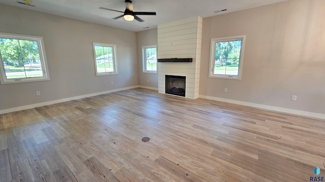 unfurnished living room featuring light hardwood / wood-style floors, a fireplace, ceiling fan, and a wealth of natural light